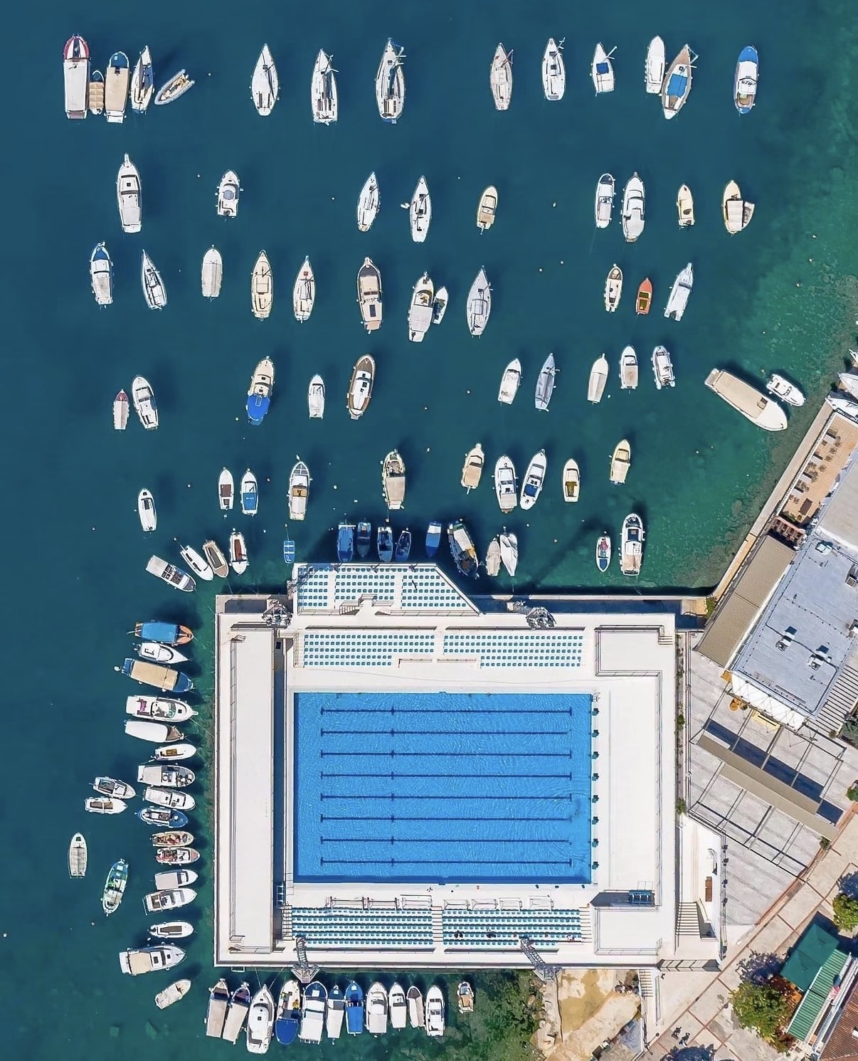 Aerial view of Herceg Novi's open-water pool complex ringed by moored boats